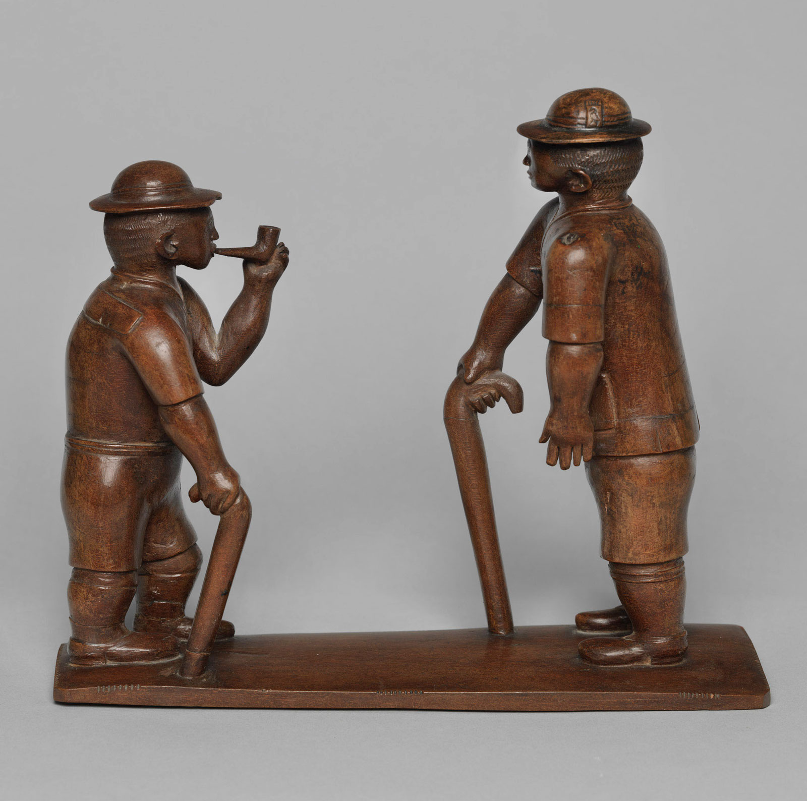 Kamba artist: Two European figures standing on a base, one with a stick and the other holding a pipe, circa 1900