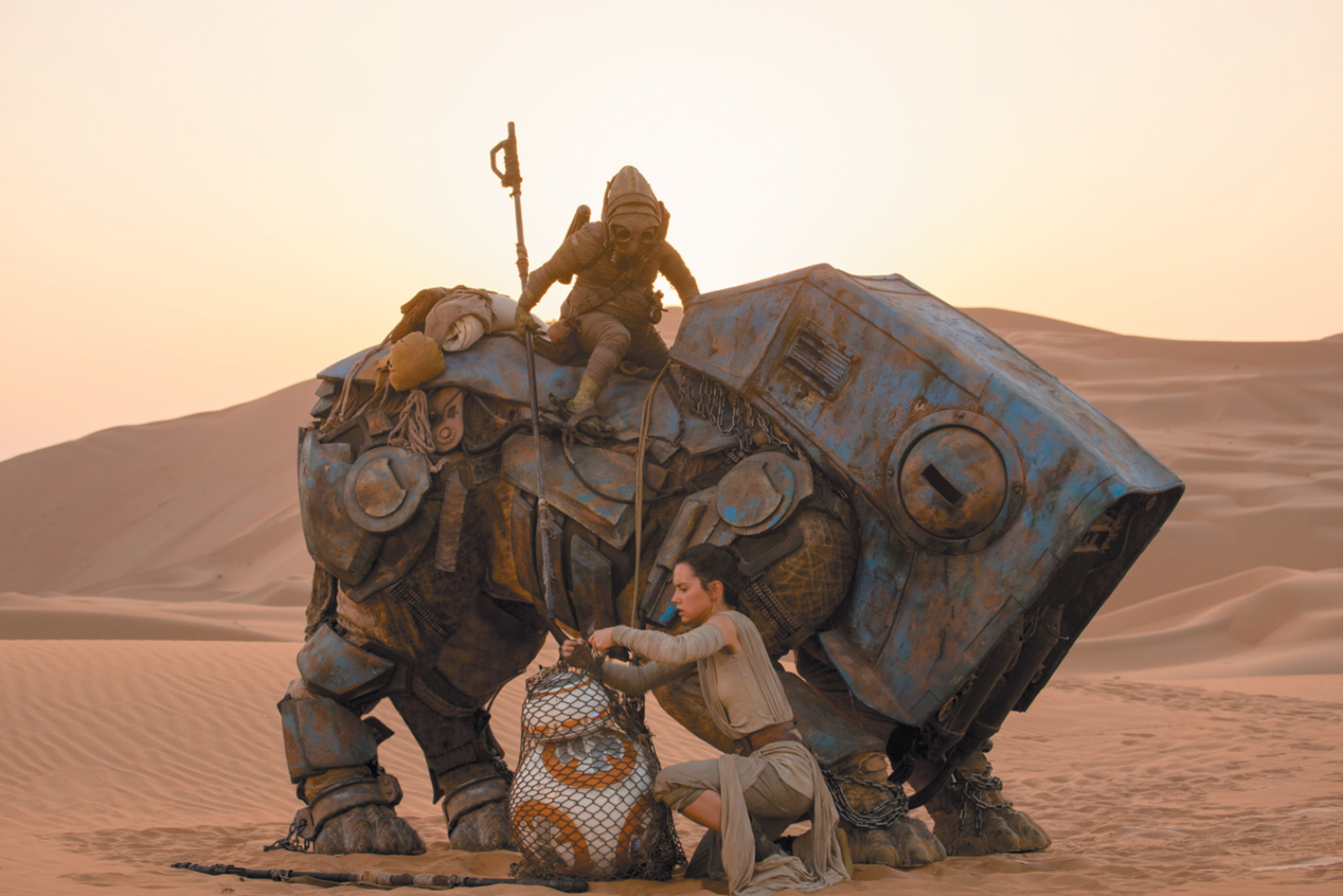 Rey (Daisy Ridley) freeing the droid BB-8 from the net of the scavenger Teedo and his semi-mechanical Luggabeast in Star Wars: The Force Awakens
