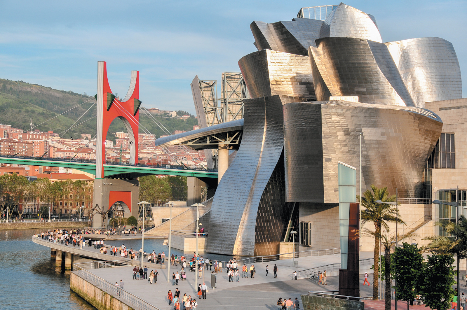 The Guggenheim Museum in Bilbao, Spain, designed by architect Frank Gehry. At left are the Nervión River and La Salve Bridge, adorned with Daniel Buren’s artwork Red Arches (2007), commissioned for the museum’s tenth anniversary.