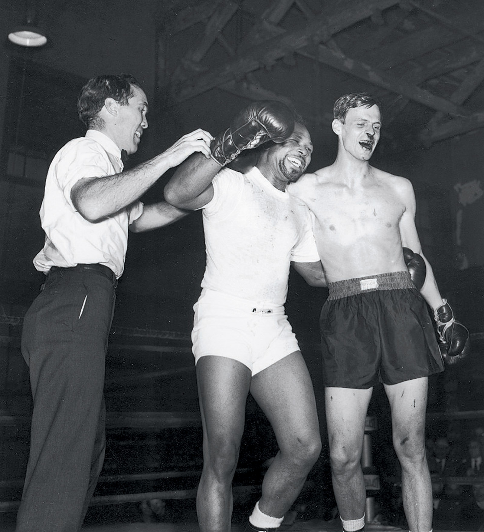 George Plimpton, right, after a boxing match with Archie Moore at Stillman’s Gym, New York City, 1959; Ezra Bowen, the Sports Illustrated editor who acted as referee, is at left. ‘Quite visible are the effects Archie Moore left on the author’s nose,’ Plimpton writes in Shadow Box, ‘what would have been described in the jaunty style of the mid-nineteenth century as follows: “Archie dropped a hut’un on George’s sneezer which shook his ivories and turned the tap on.”’