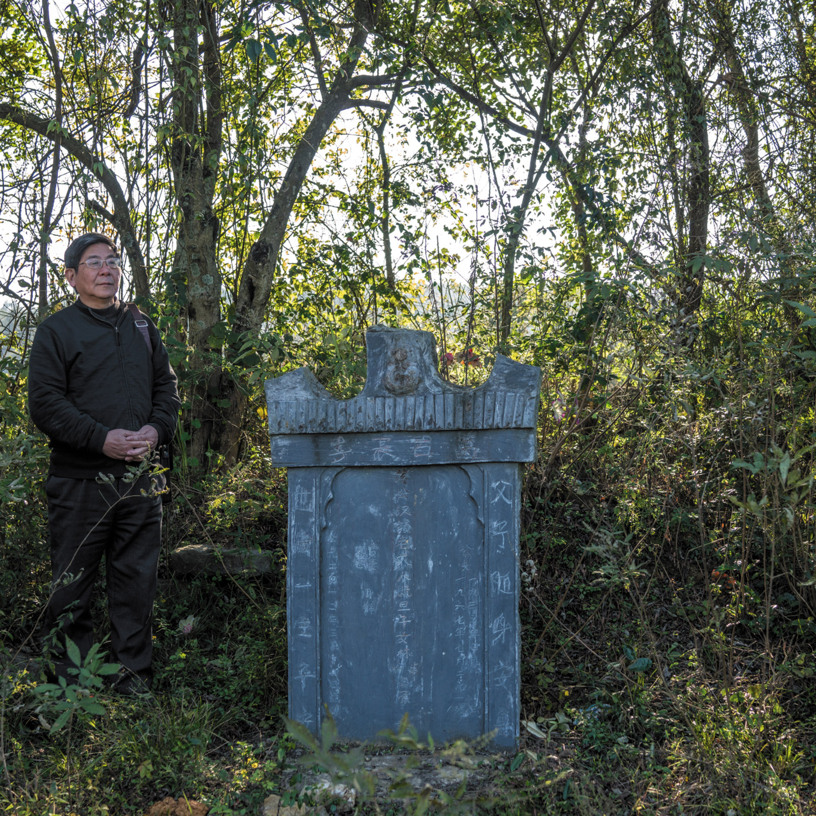 Tan Hecheng at a tombstone put up by Zhou Qun for her husband and three children, who were among the thousands of people killed during the Cultural Revolution in Dao County, southern China, November 2016; photograph by Sim Chi Yin