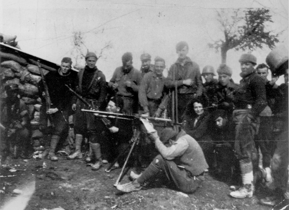 George Orwell (standing behind the machine-gunner) and his wife Eileen (crouching at Orwell’s feet) with the British Independent Labour Party contingent at the Huesca Front during the Spanish Civil War, March 1937