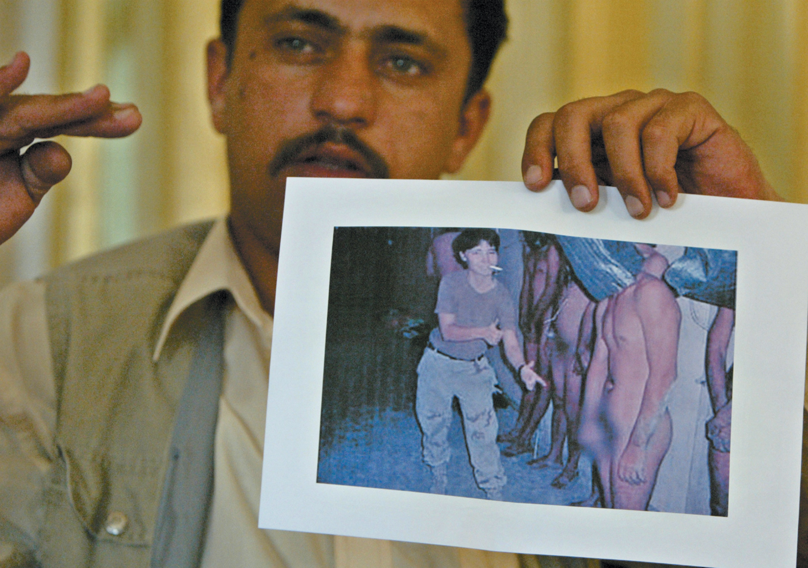 Saddam Saleh, a former prisoner at Abu Ghraib, showing a photograph of himself and other prisoners being abused there in November 2003 by US soldiers, Baghdad, May 2004
