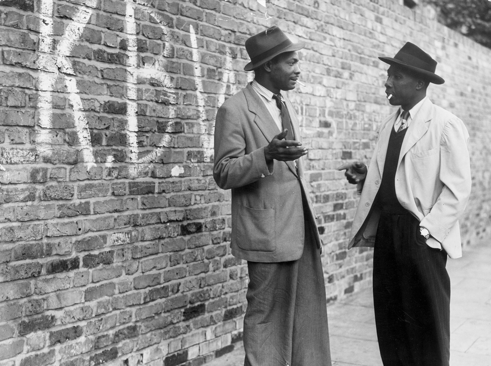 Two men talking in a Brixton street; in the background, the graffiti stands for “Keep Britain White,” London, June 9, 1952