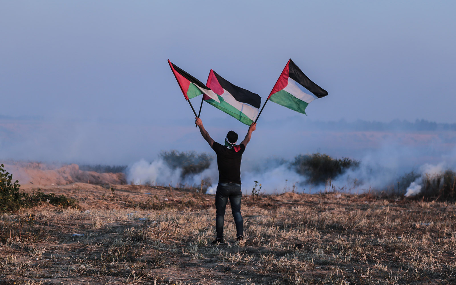 A Palestinian waving flags as tear gas disperses from canisters fired by Israeli troops during a protest near Khan Younis, Gaza Strip, March 22, 2019