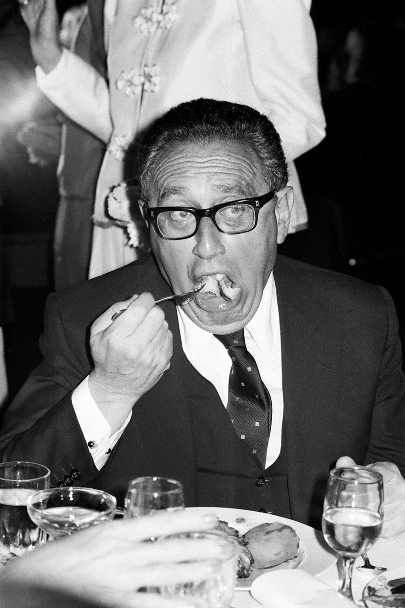 Photograph of Henry Kissinger eating at a table