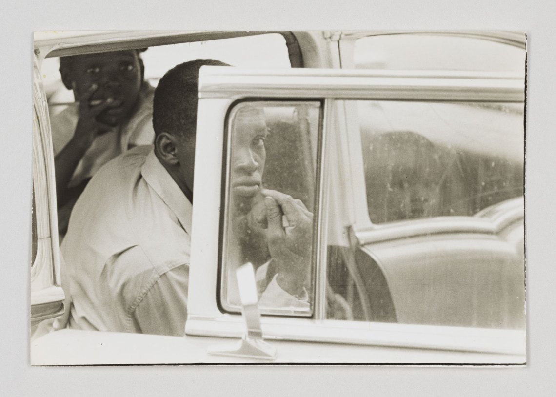 Three boys seen through the window and open door of a parked car