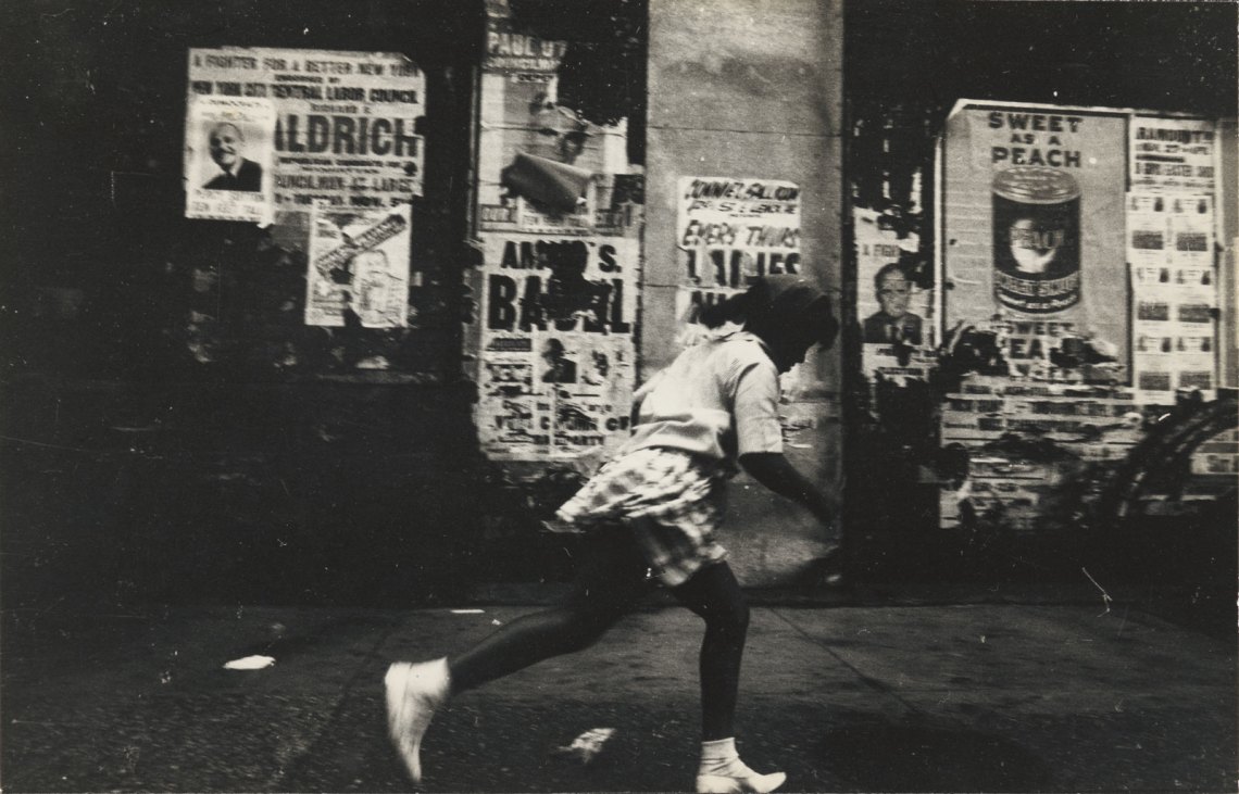 A girl caught in motion running, behind her the peeling posters for Sweet As a Peach and other advertisements
