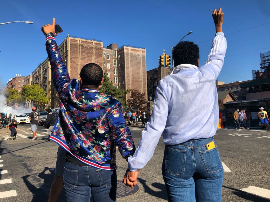 Two women holding hands with their backs facing the camera, cheering toward the street