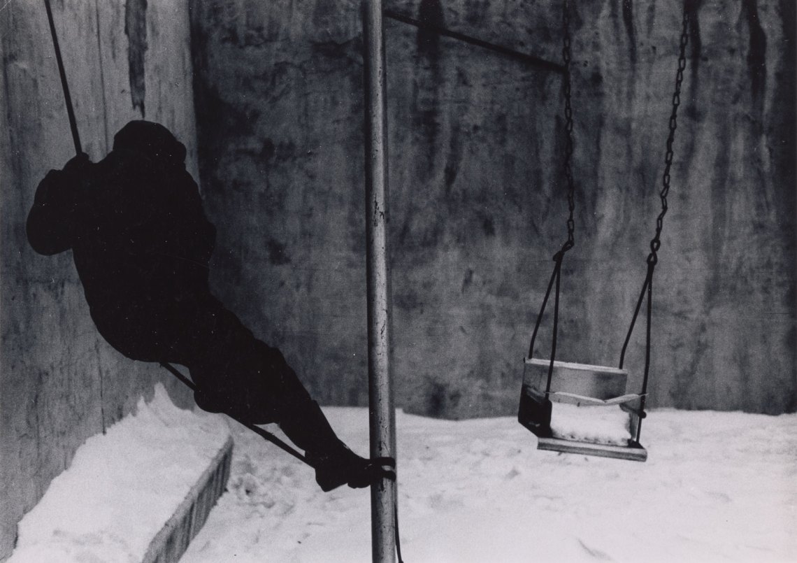 A boy in dark shadows on a swing in the snow
