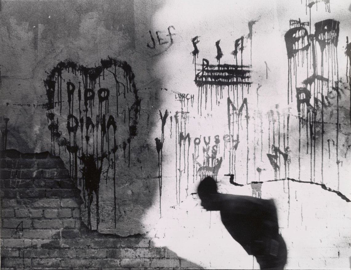 Graffiti bleeding down a wall, as a stooped man passes by