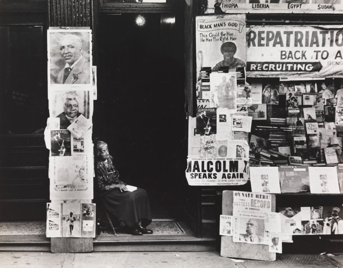 A woman sitting in a doorway nearby a newsstand