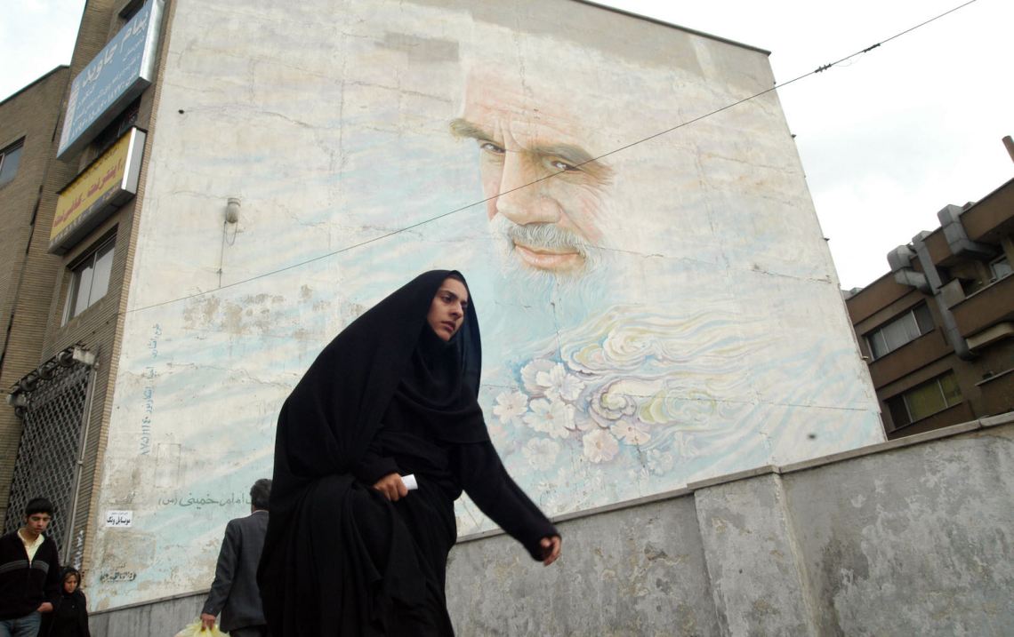 A woman passing by a mural of Ayatollah Khomeini