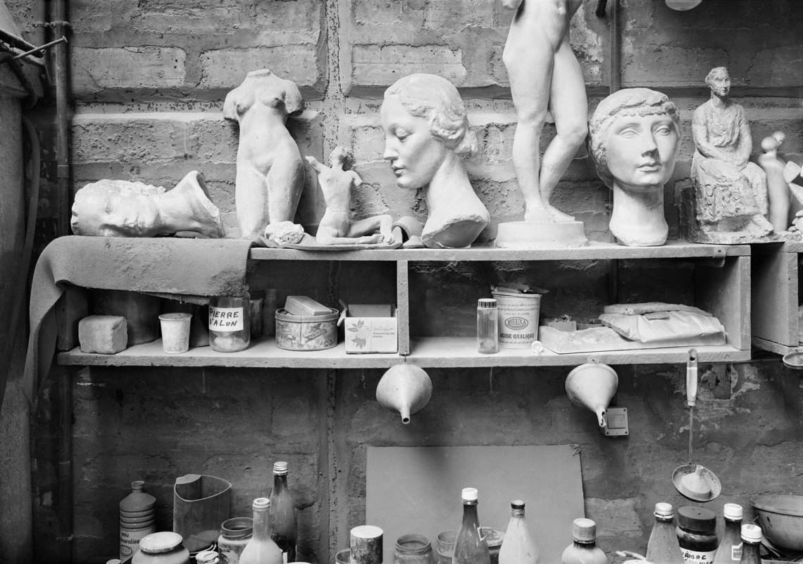 Sculptures of busts and body parts sitting on a shelf, in black and white