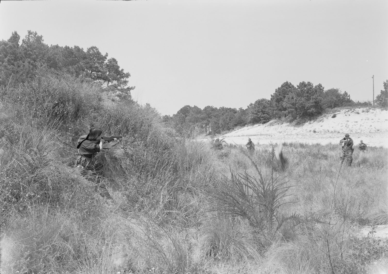 A person crouching in grasses aims a sniper