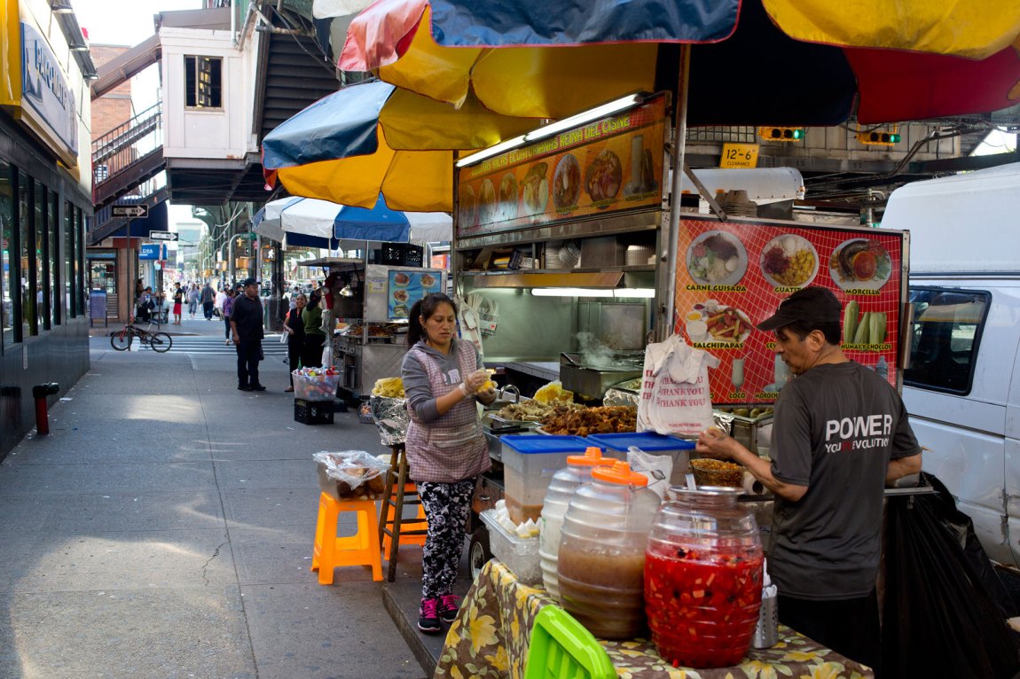 Two people selling food and drink from a cart on the side of a busy street