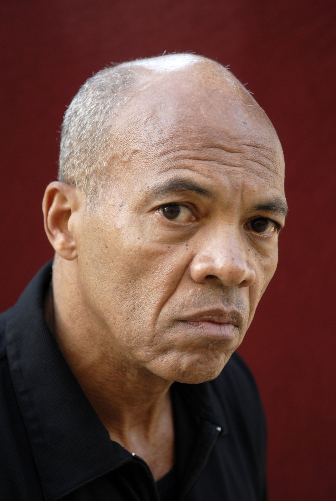 A close-up image of the writer John Edgar Wideman from the chest up in front of a red background