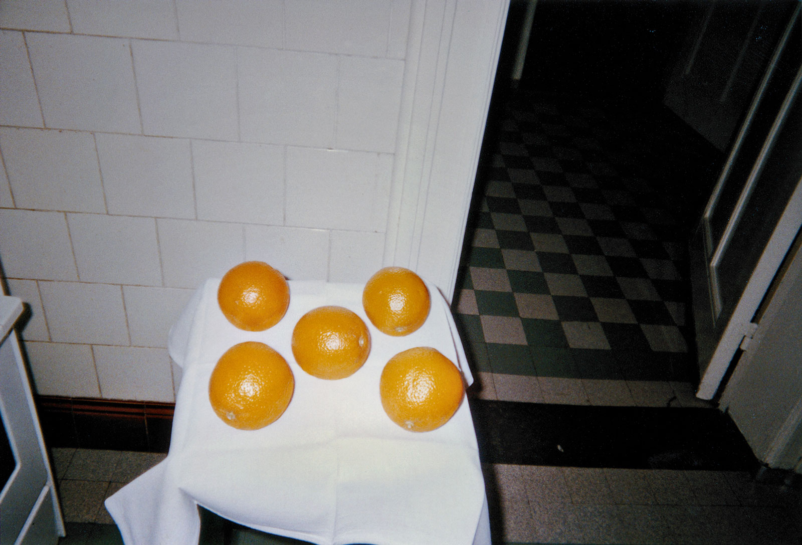 five oranges on a small white-clothed table in what appears to be a tiled kitchen