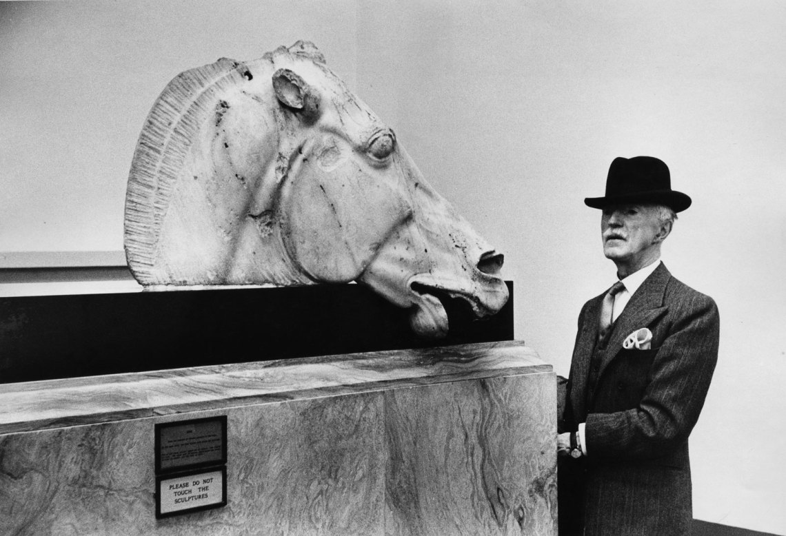 a man in a hat looking at a large horse head sculpture inside the museum