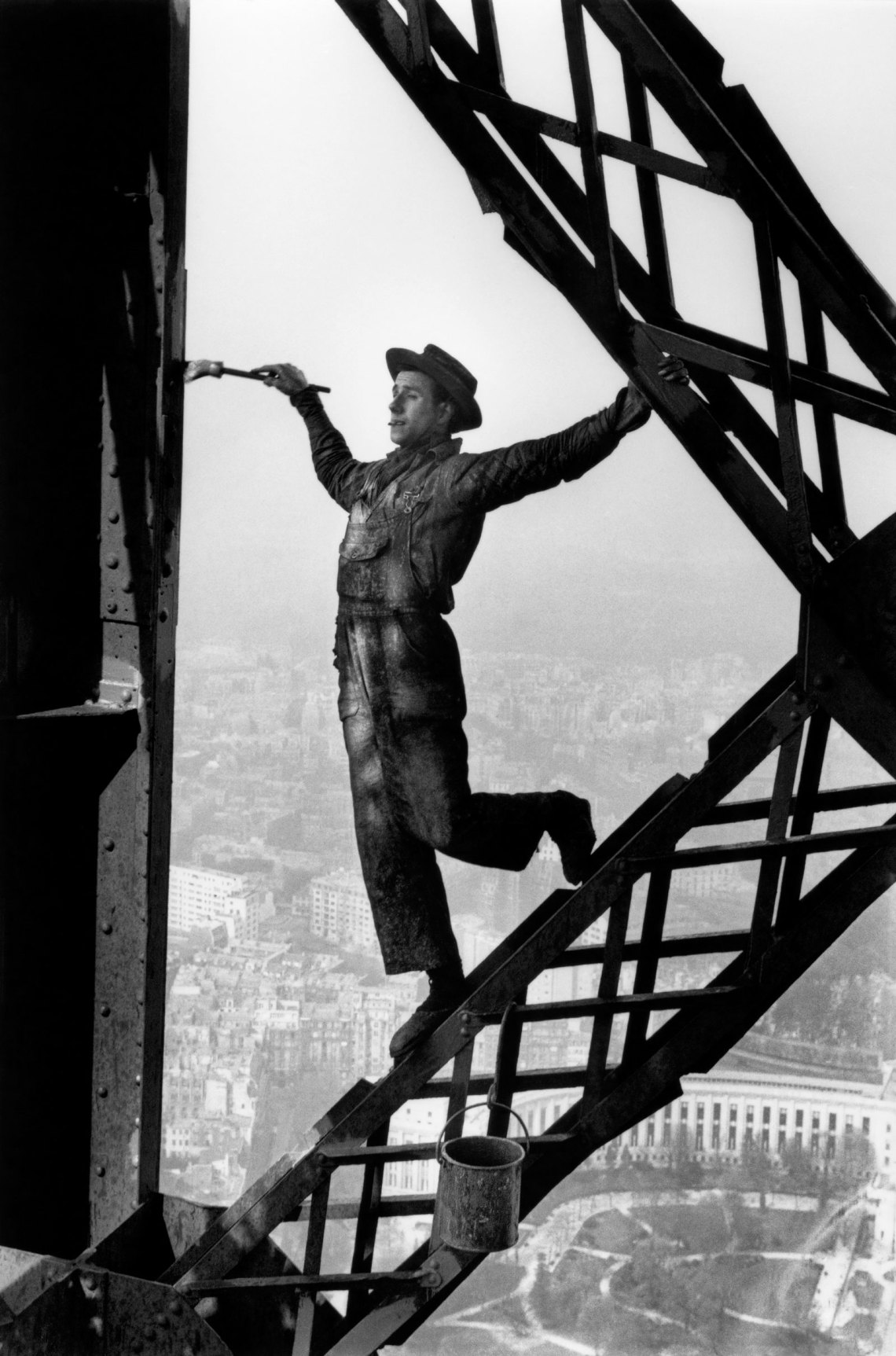 black and white image of a painter with one leg up balletically, his brush poised to bank the iron beam of the Eiffel Tower