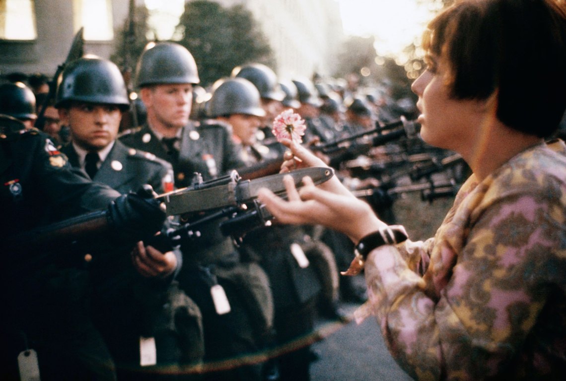 color image of a teenager holding a flower to the bayonets of police
