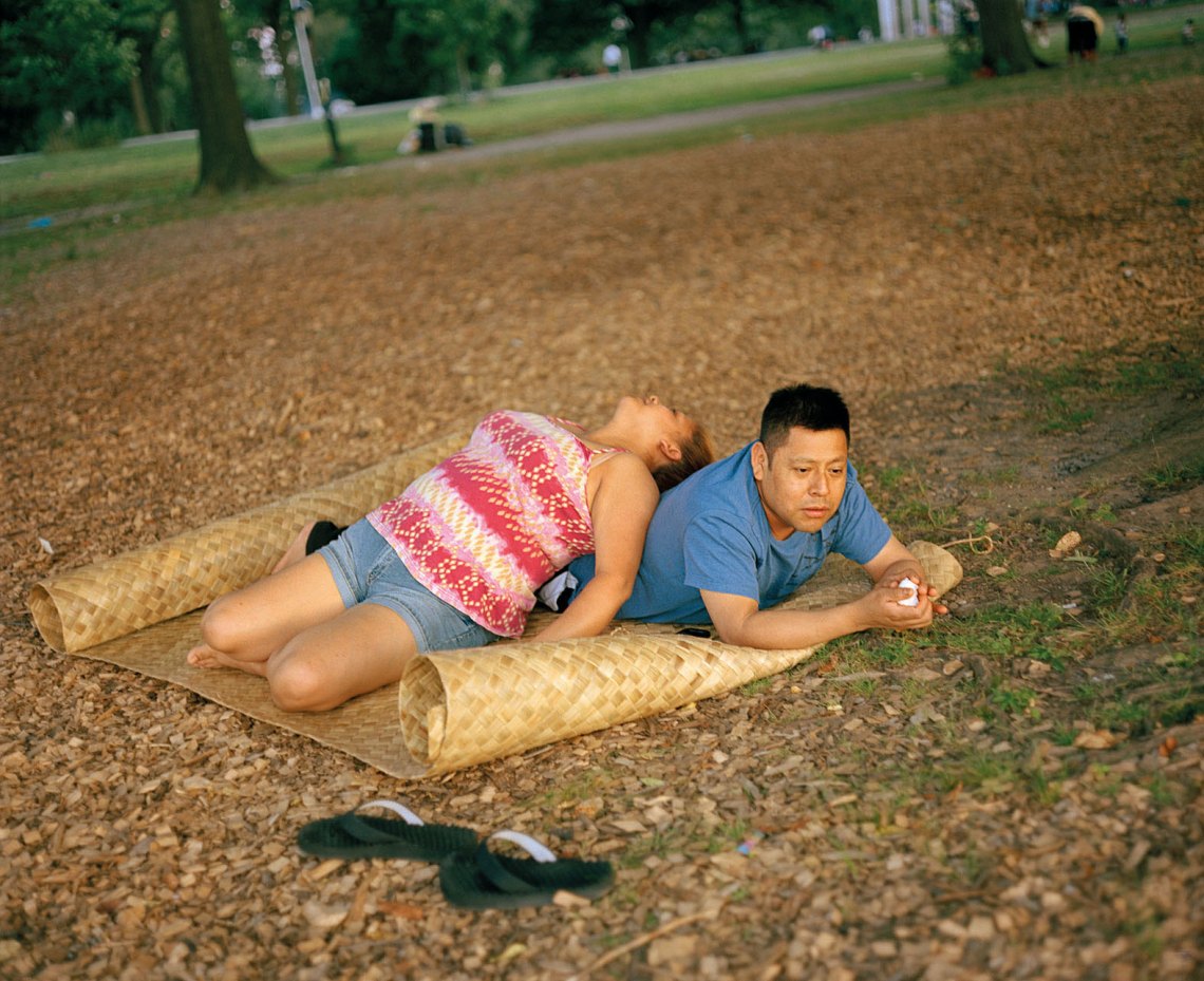 A woman leans against a man on a mat, lying down in the park