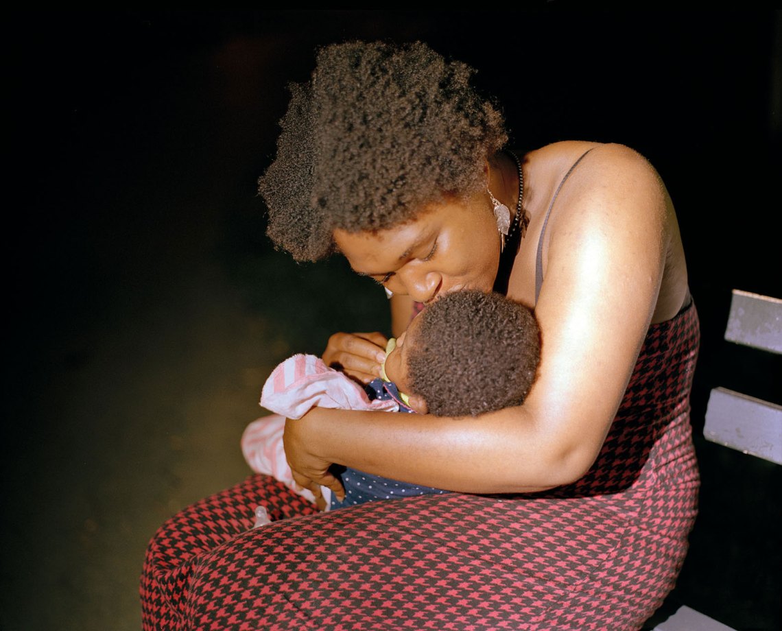 an African American woman kisses her baby at night on a bench