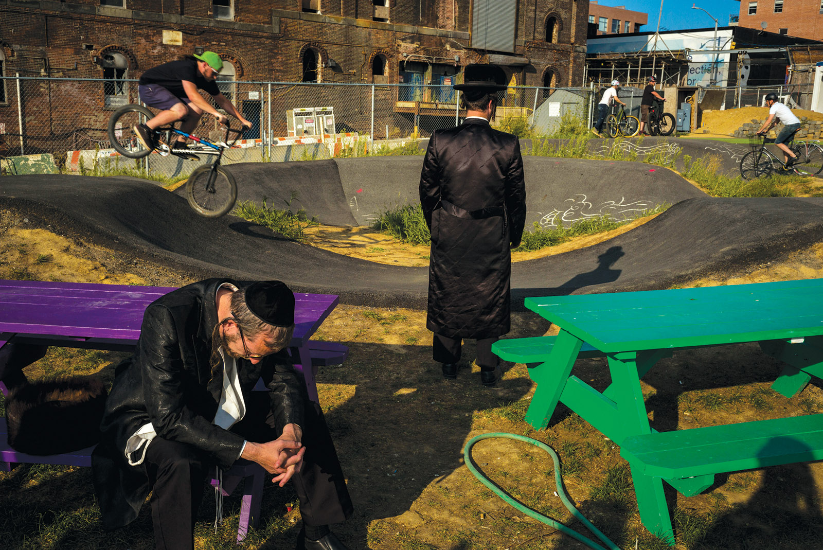 Two Hasidic men in a Williamsburg open lot with cyclists and picnic tables