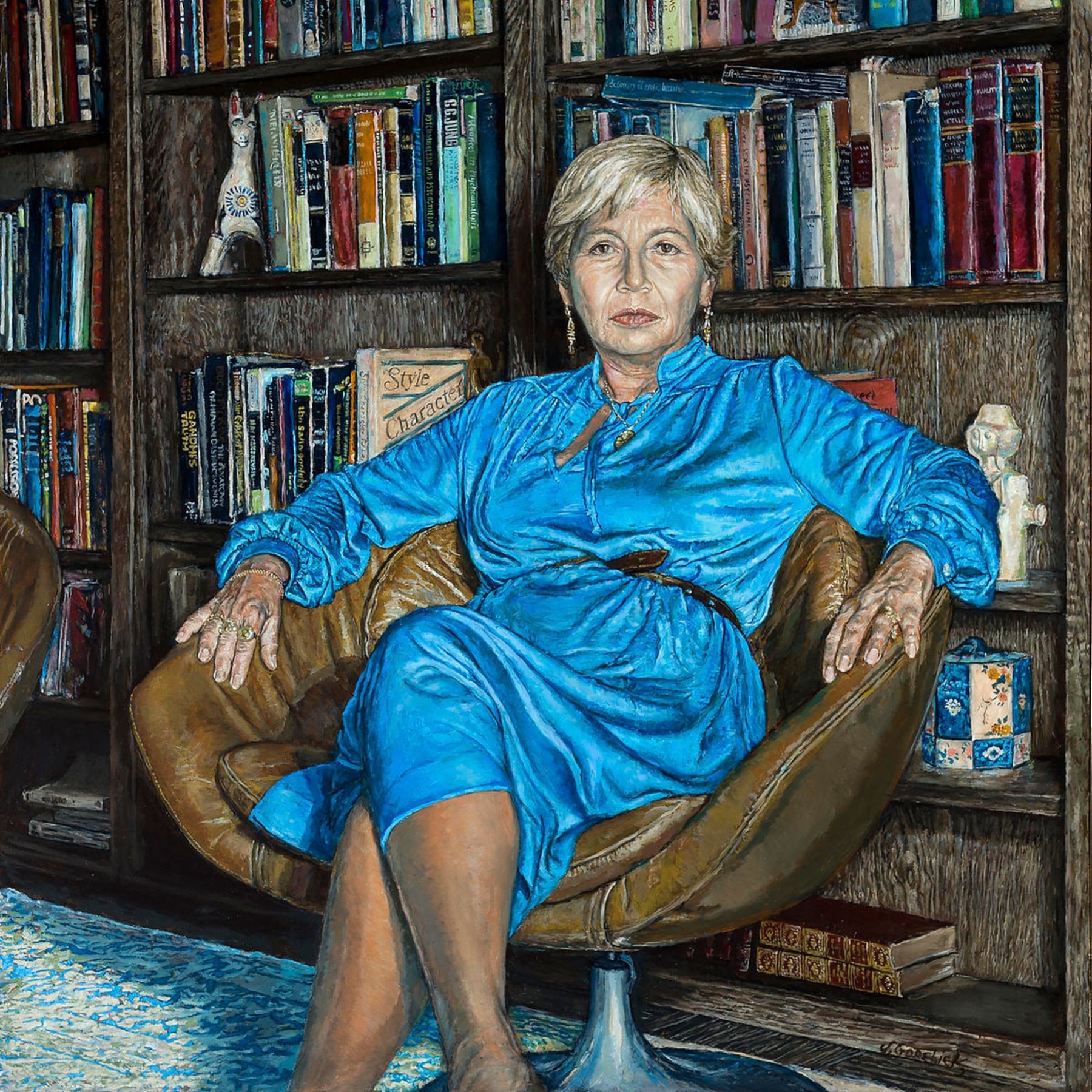 Woman in a blue dress sitting in a leather chair in front of a bookcase