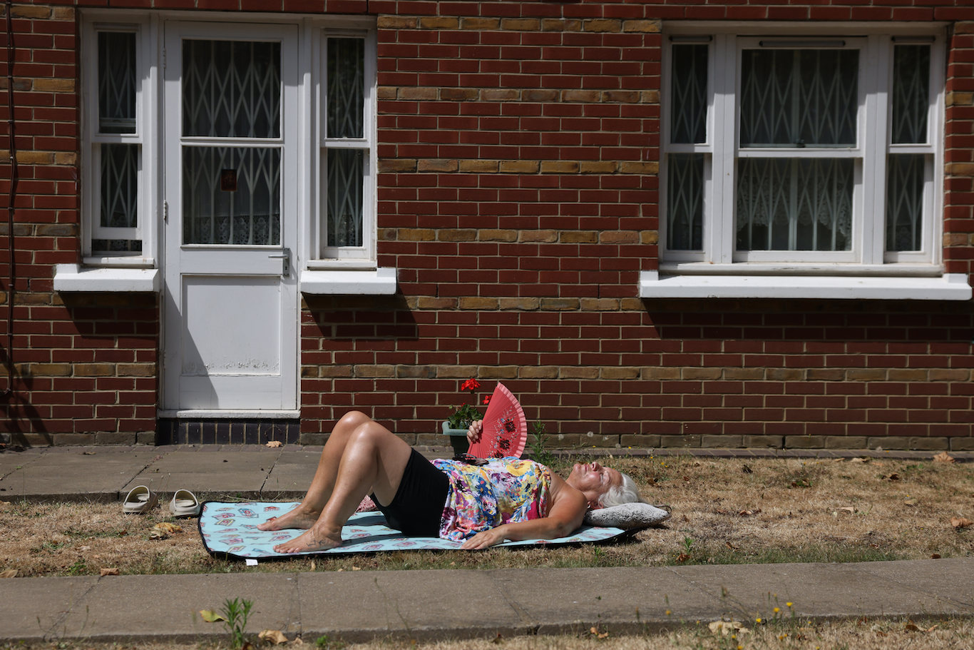 A woman lies on a towel with a handheld fan outside her home in Hackney, London