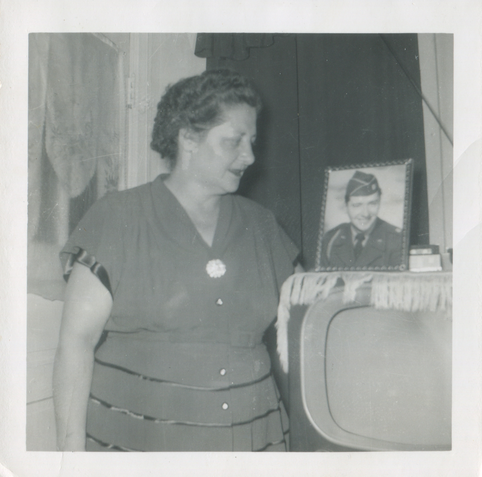 Woman gazing at framed photograph of soldier atop a TV set