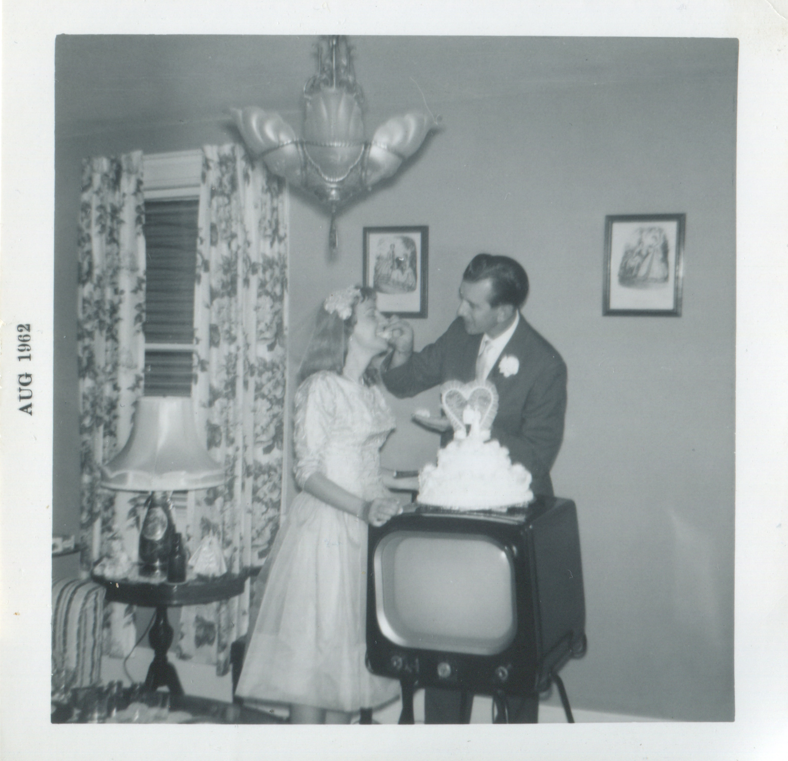 A just-married couple eating from a wedding cake atop a TV set