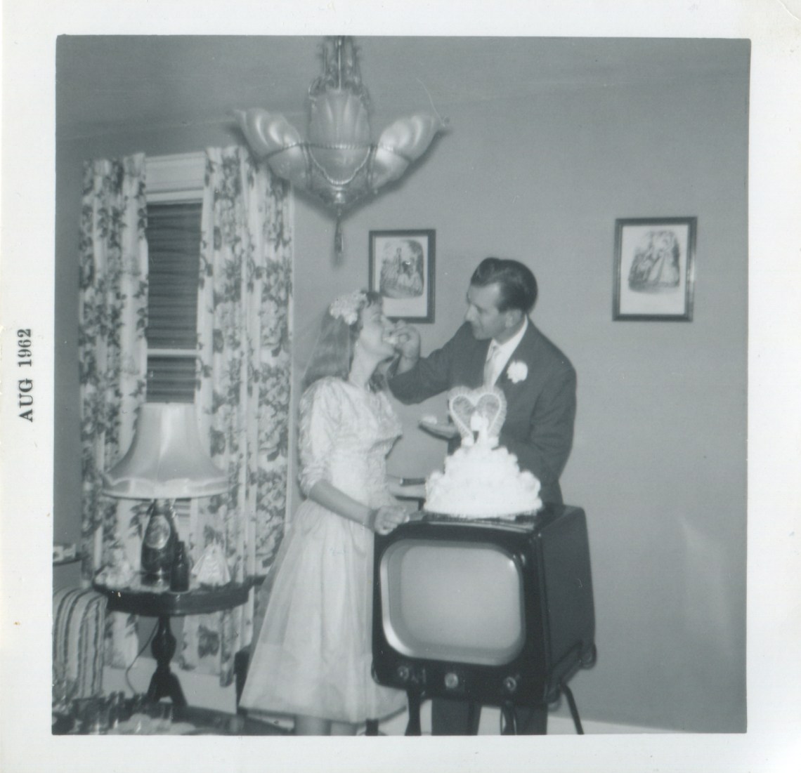 A just-married couple eating from a wedding cake atop a TV set