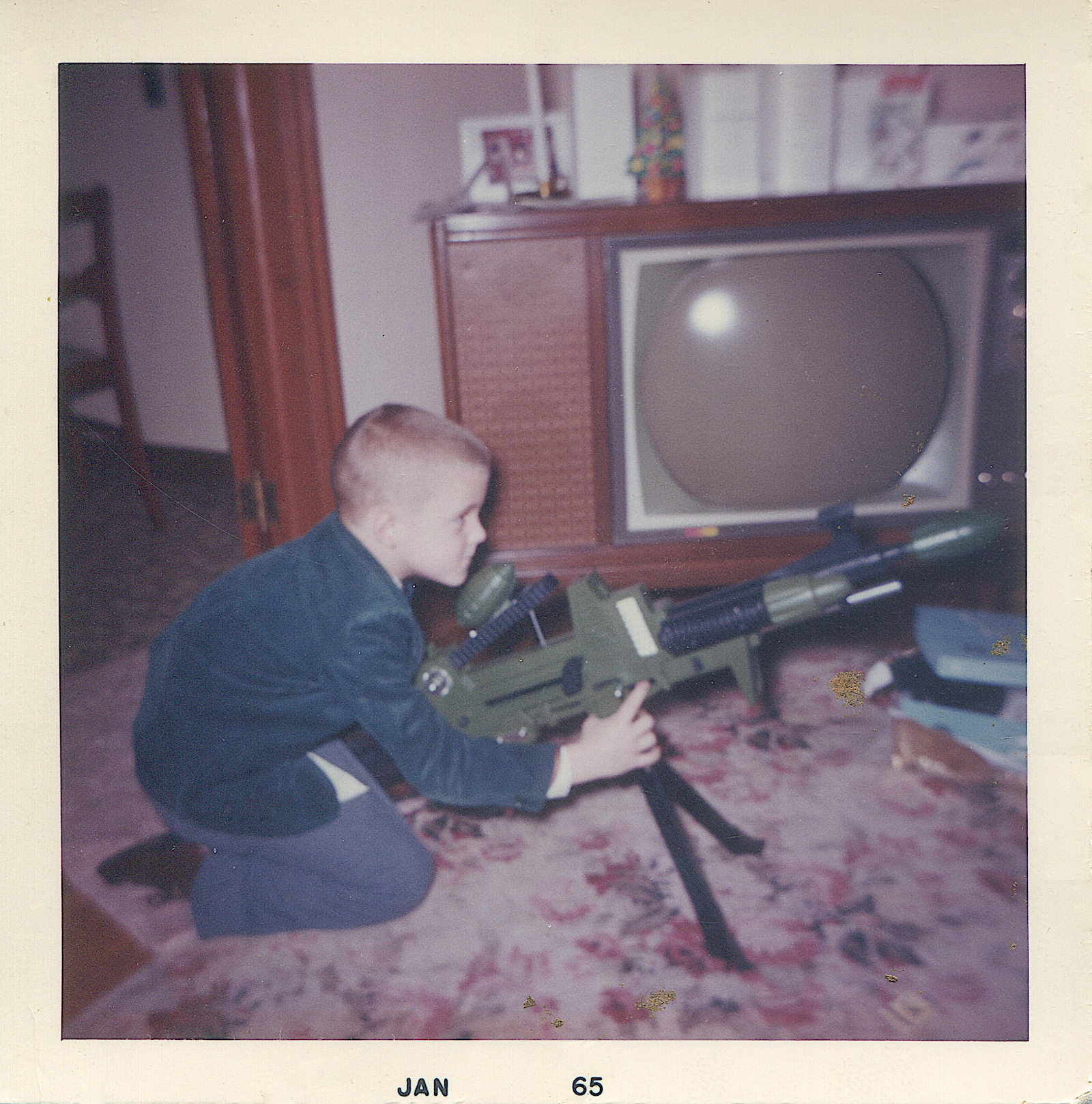 A young boy with a submachine gun in front of a TV set