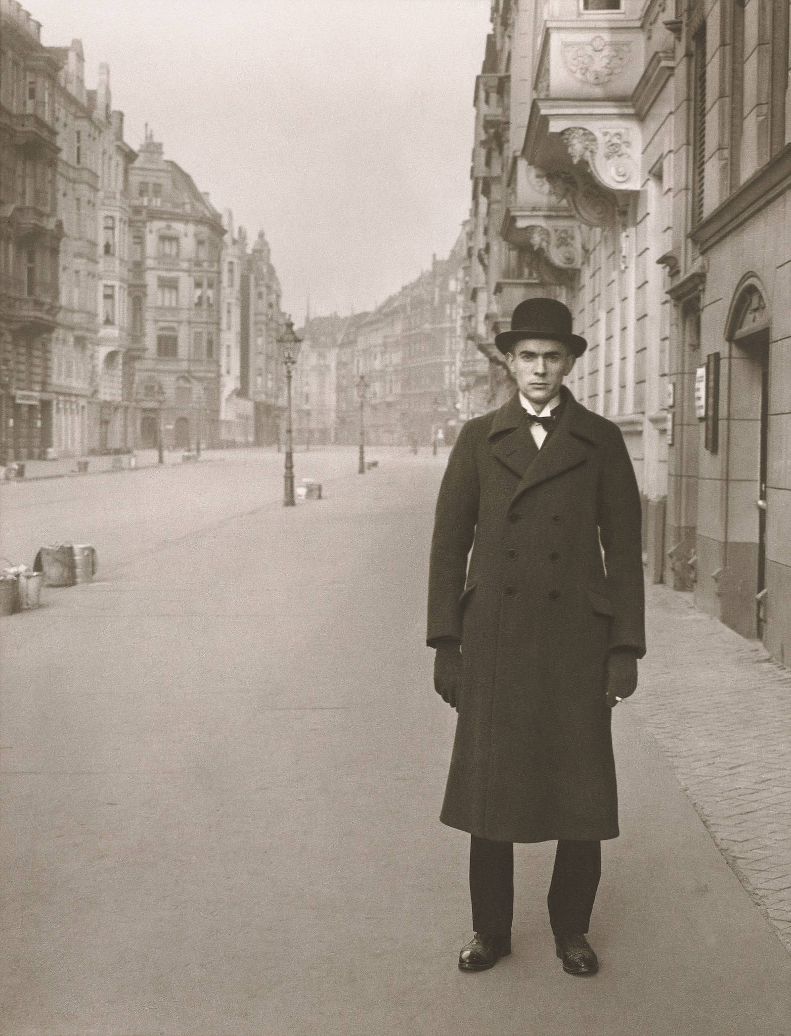 A man in a coat and a bowler hat standing on a deserted street