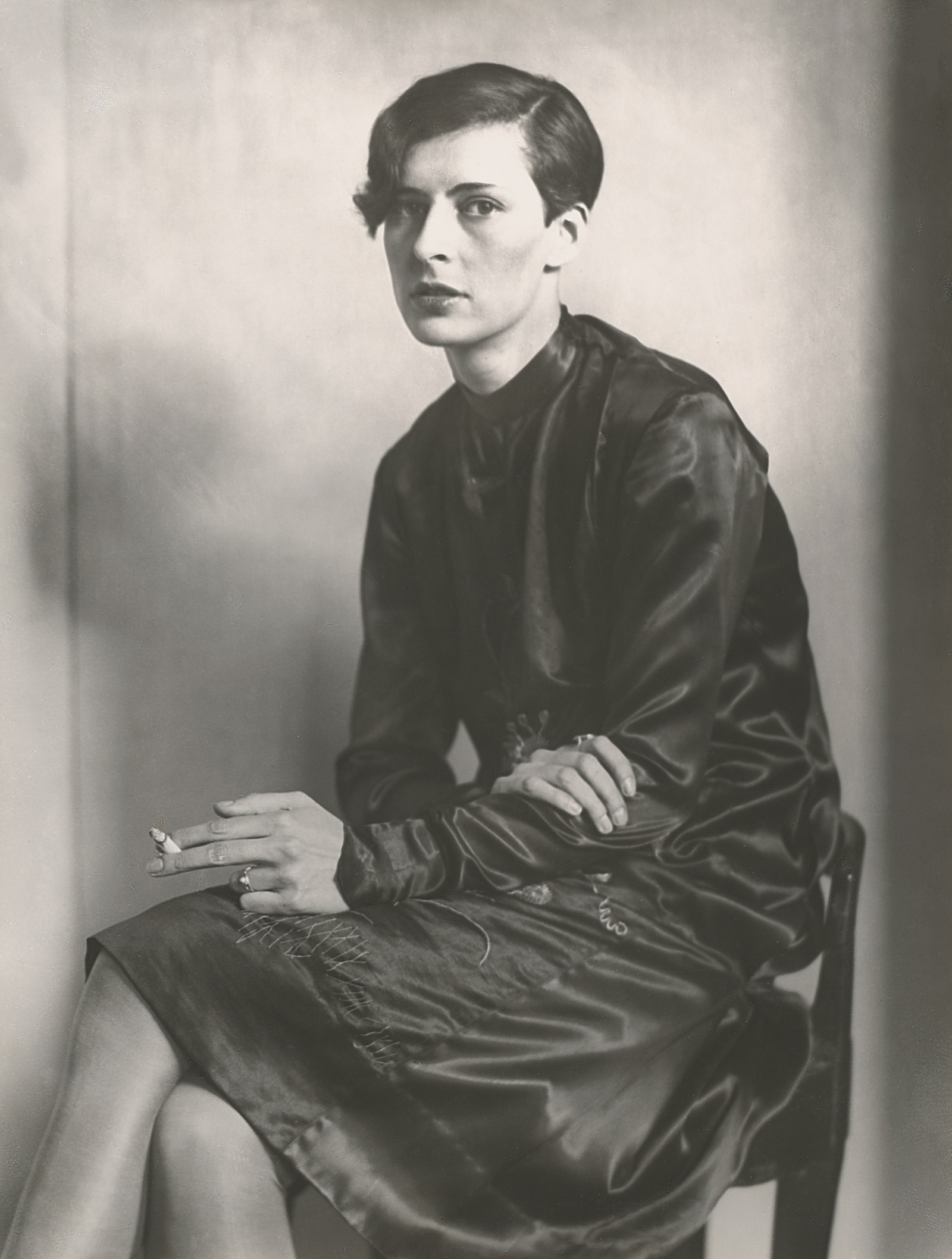 Black-and-white photograph of a young woman sitting in a chair holding a cigarette