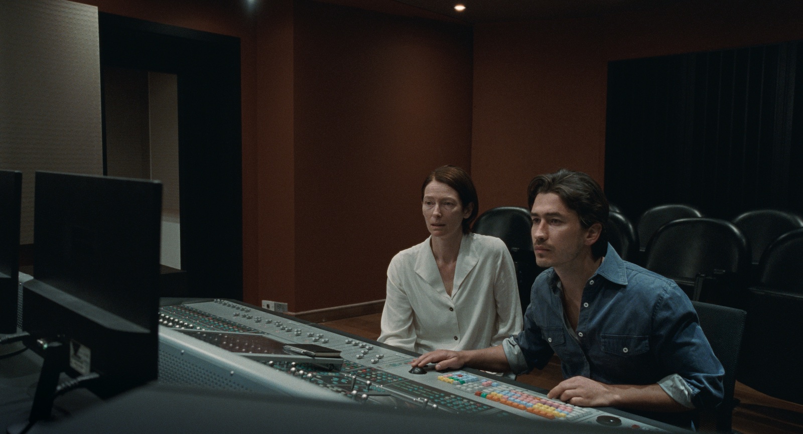 A woman and a man sit at a sound mixing board in a recording studio