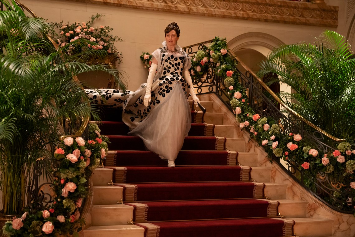A woman in Gilded Age finery descends the stairs of her ballroom