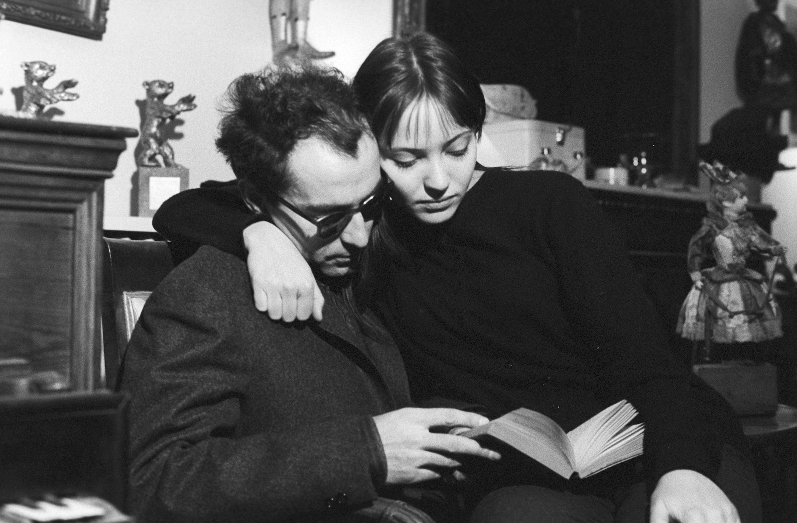 A black-and-white photograph of a man and a woman reading a book together