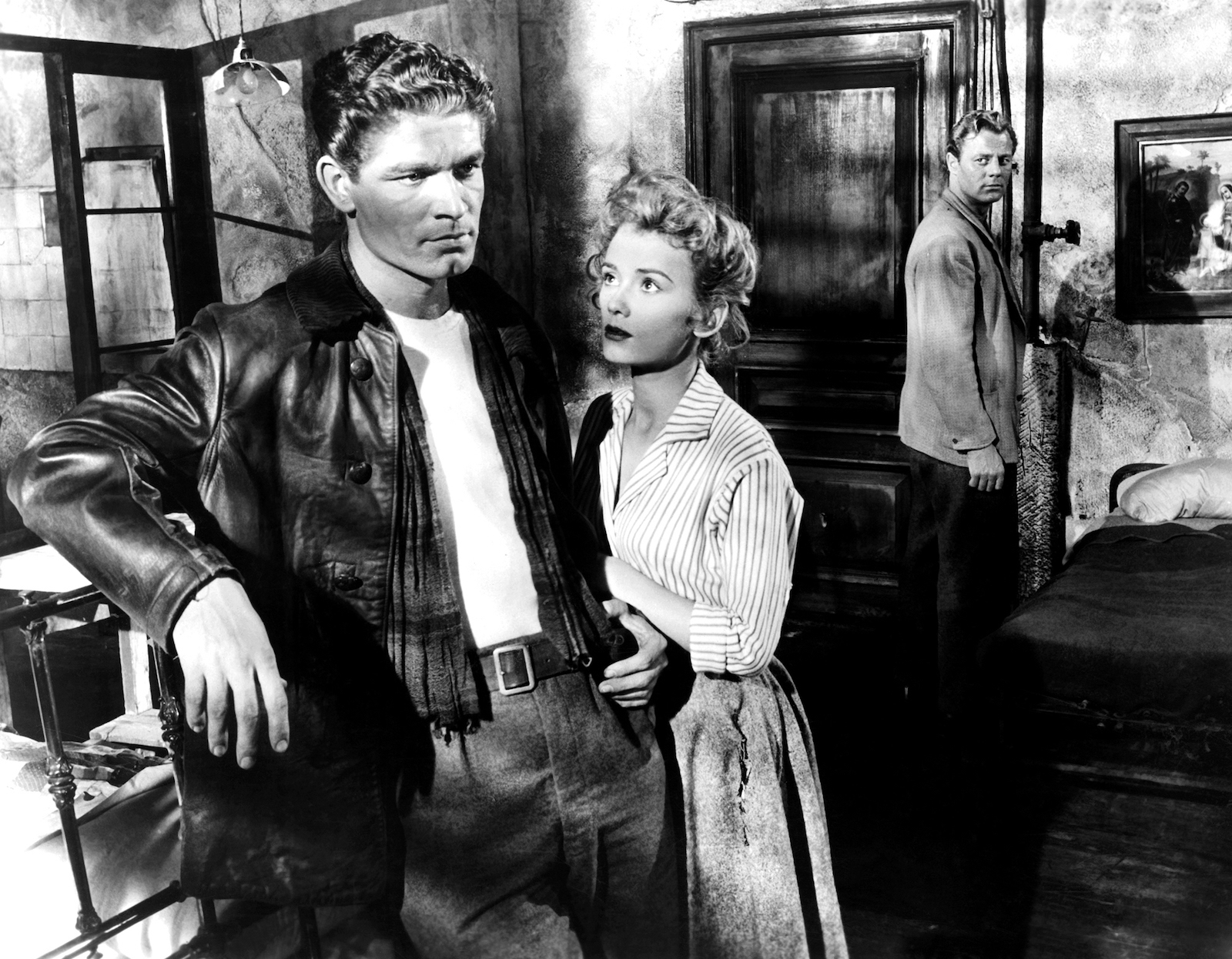 A black-and-white film still of a man staring into space while a woman gazes at him and another man looks on