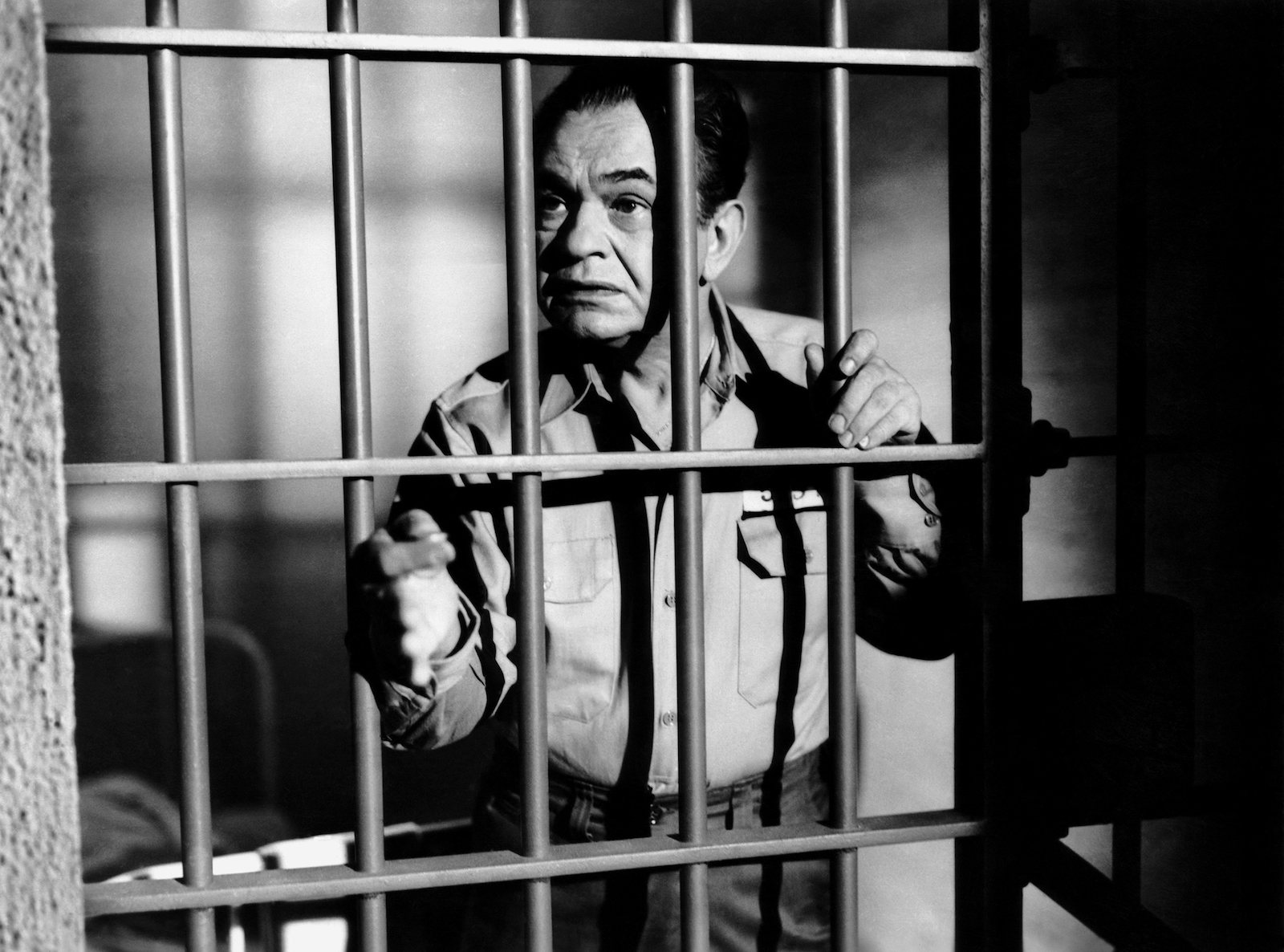 A black-and-white film still of a man behind bars