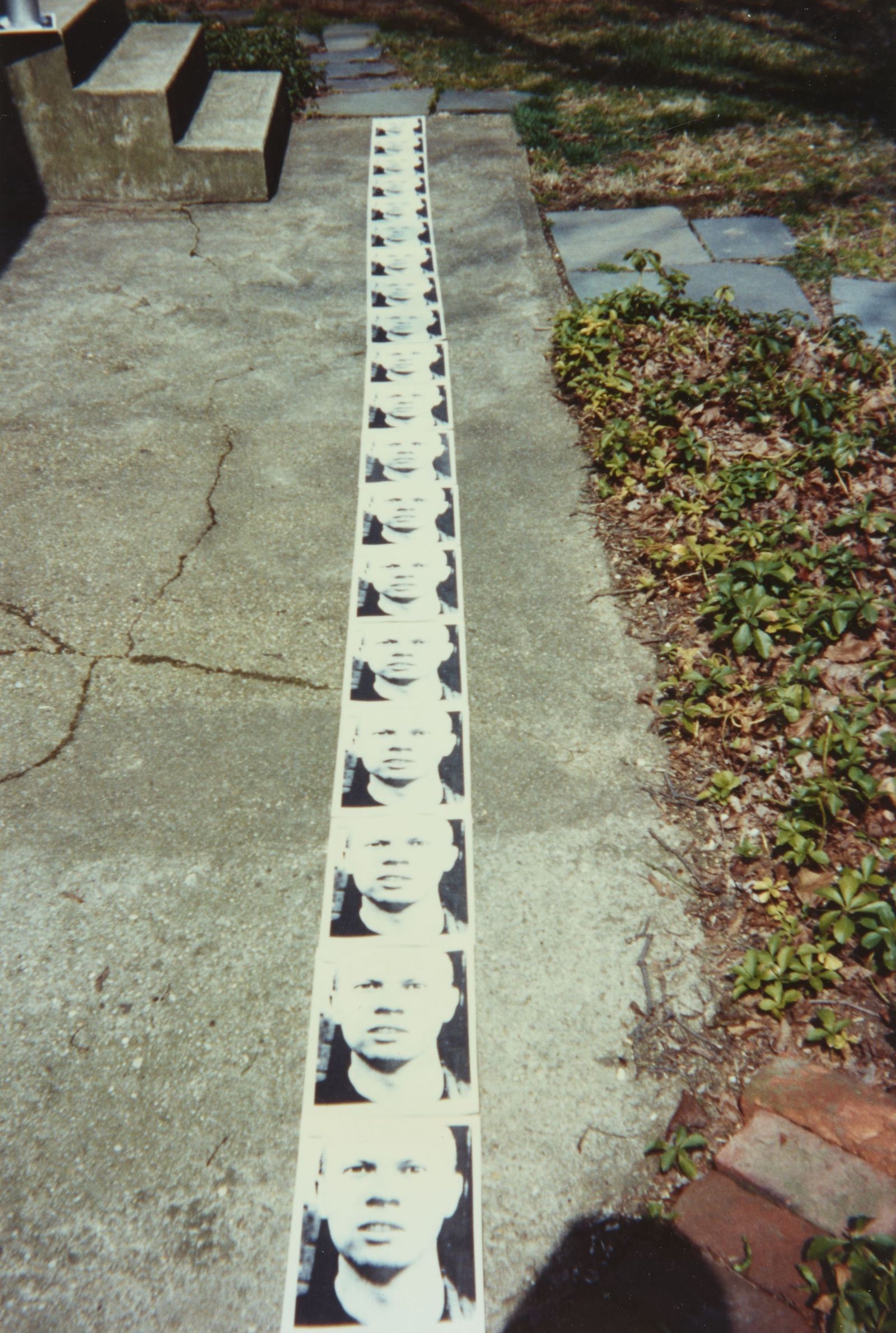 a long vertical row of photographs of the same face, extending up a sidewalk