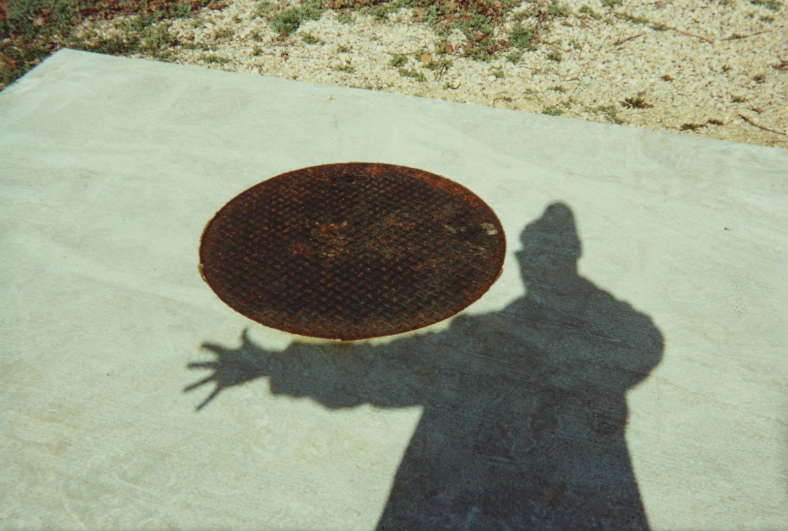 A shadow of a man extending his arm next to a manhole