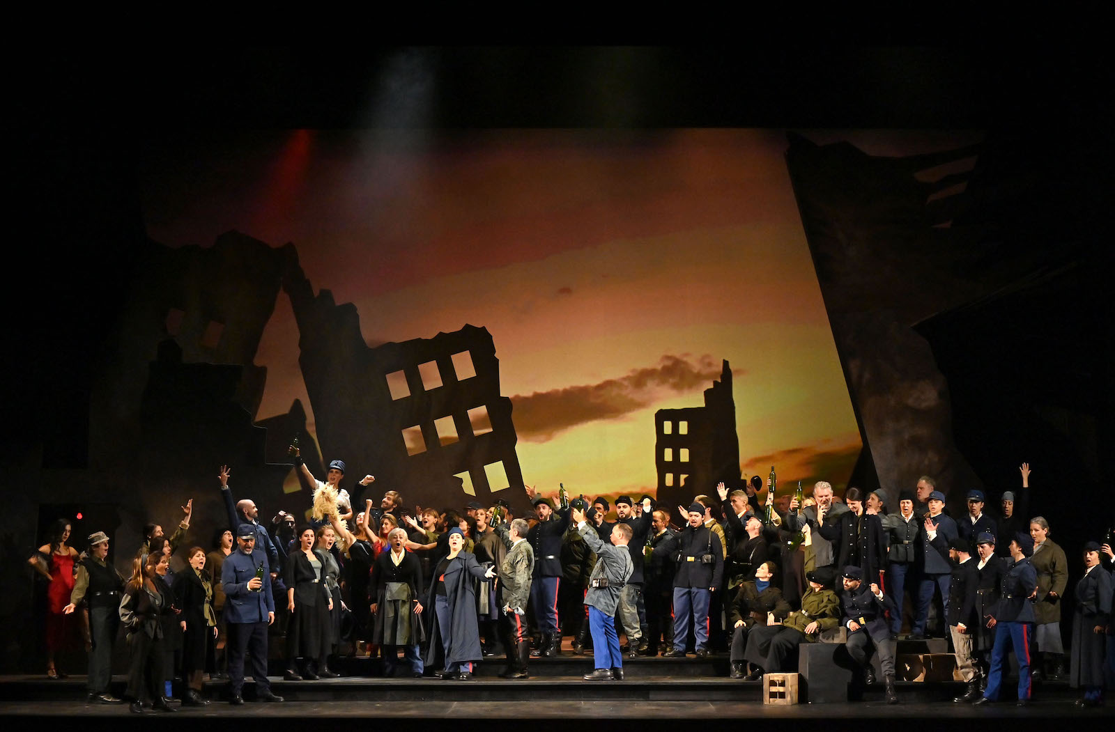 A large crowd singing onstage against a painted backdrop of a sunset
