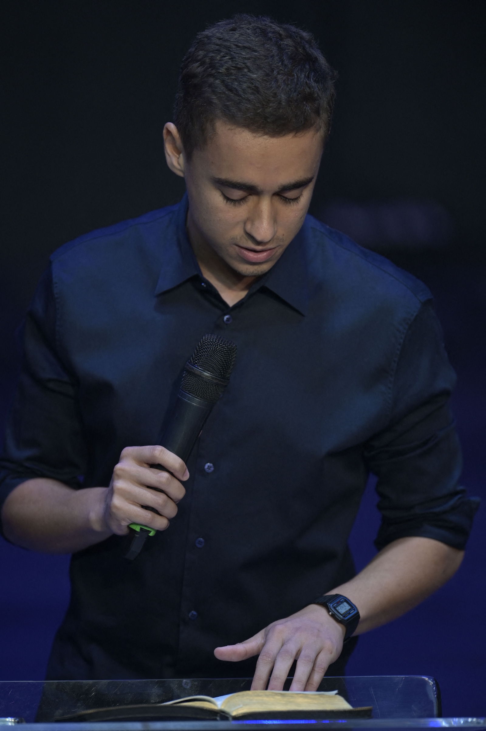 A young man reading the Bible, with a microphone in his right hand