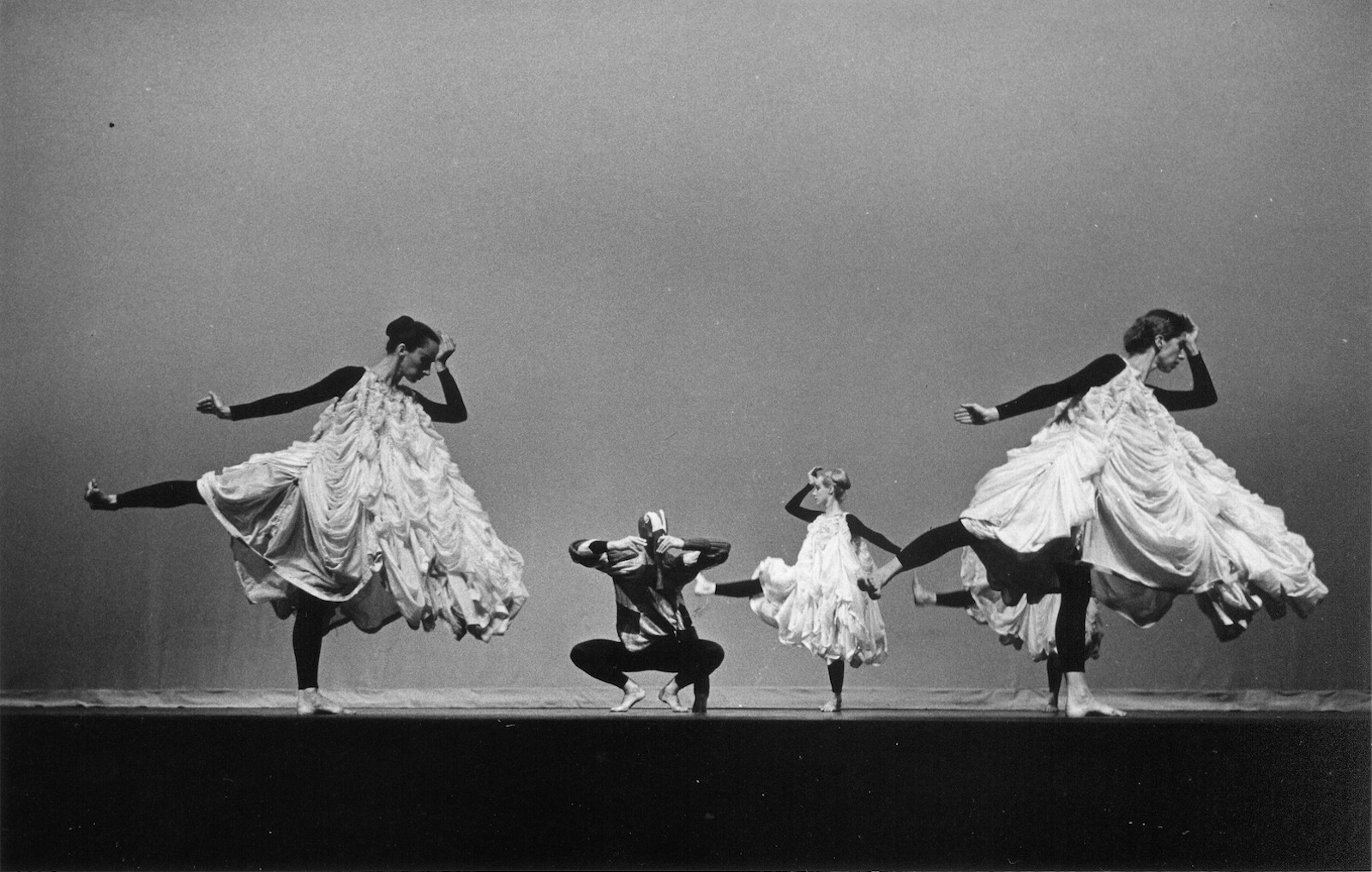 A black-and-white photo of five dancers onstage, two in the foreground with billowy costumes