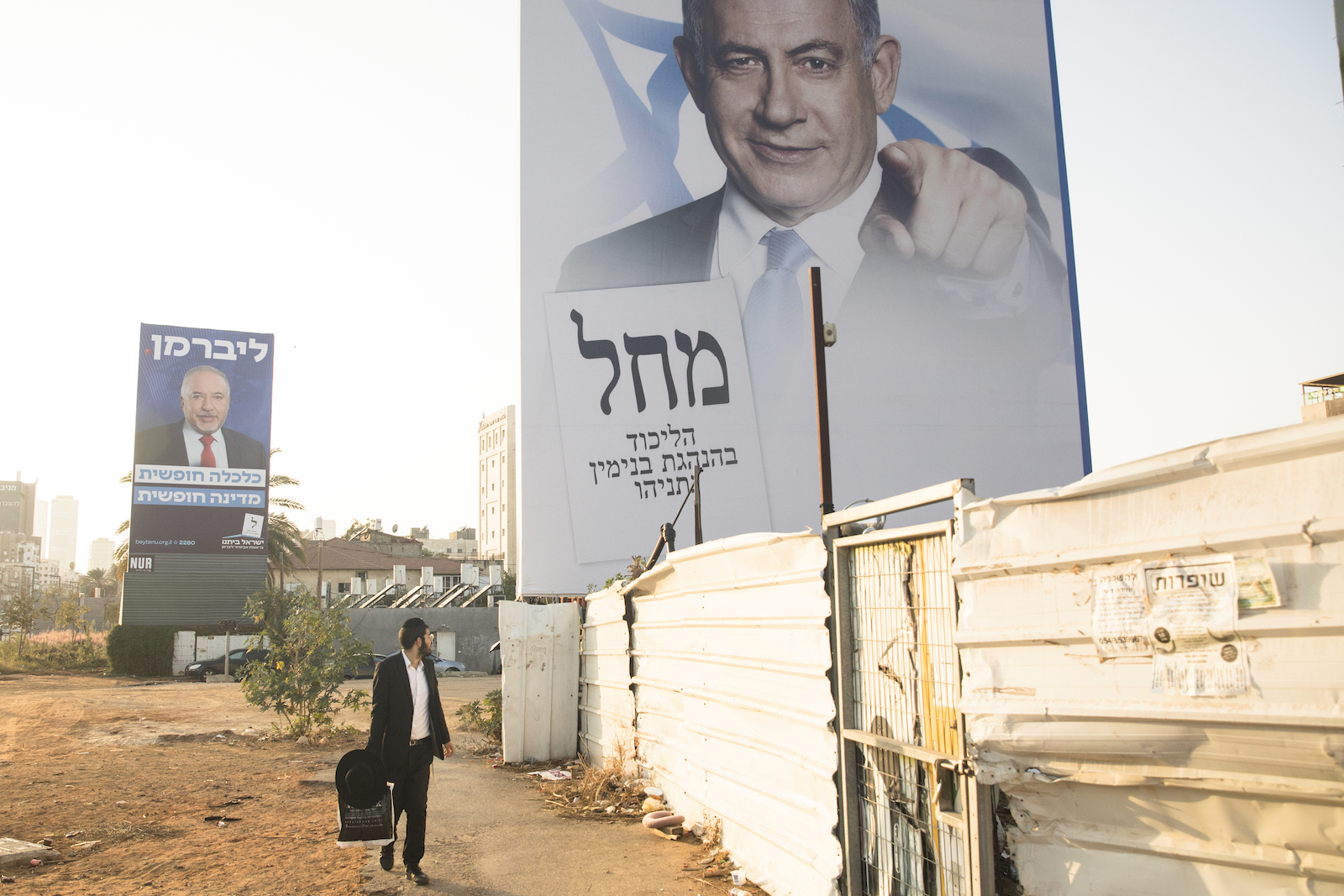 A man walking under a giant billboard, which shows another man pointing at the viewer