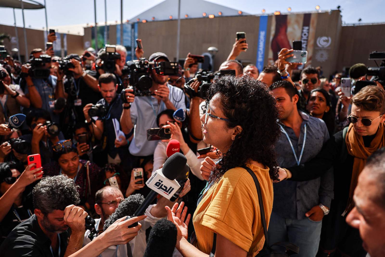 A woman addressing a packed crowd of reporters