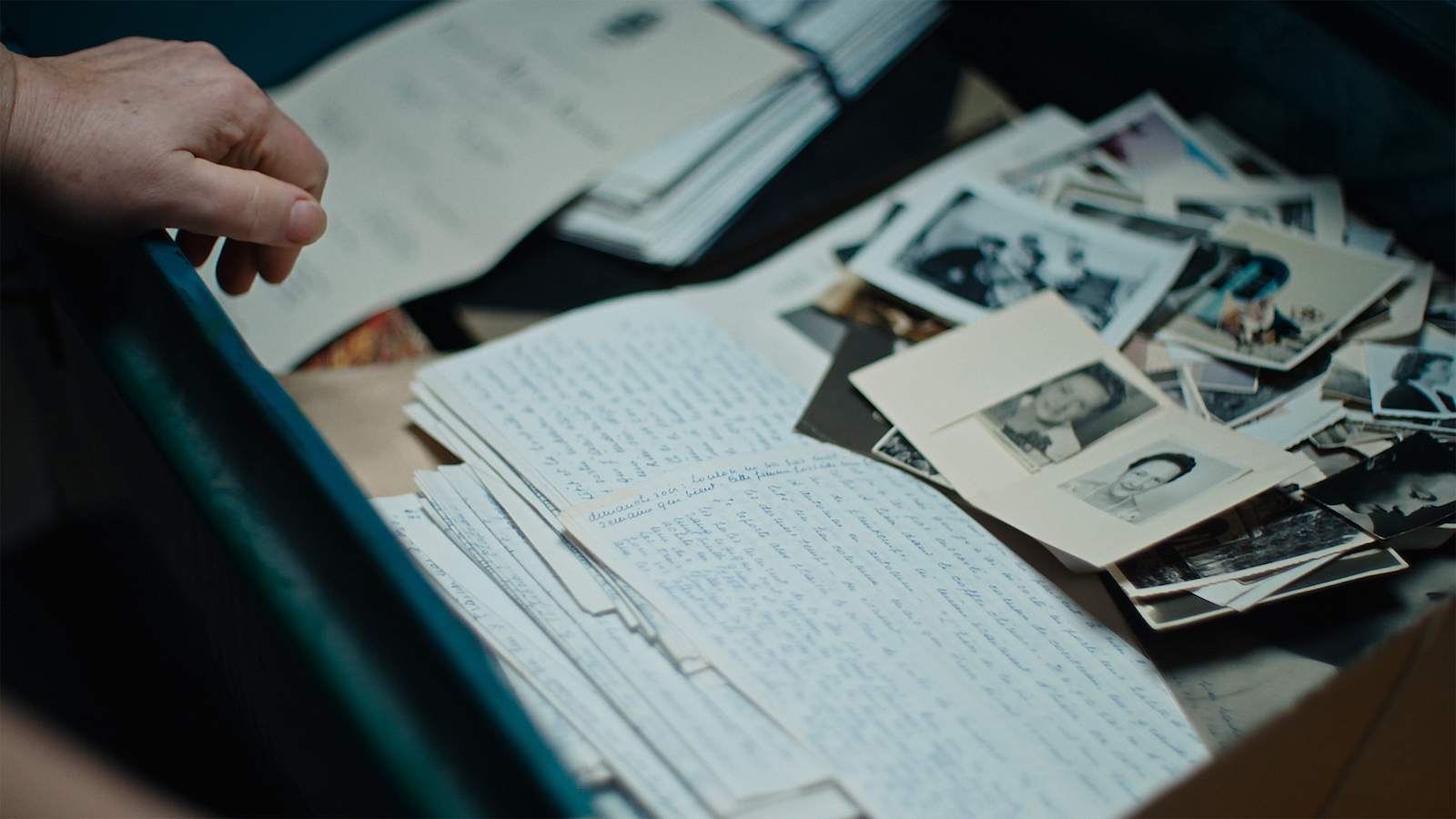 A hand hovers over a drawer full of photographs and handwritten documents