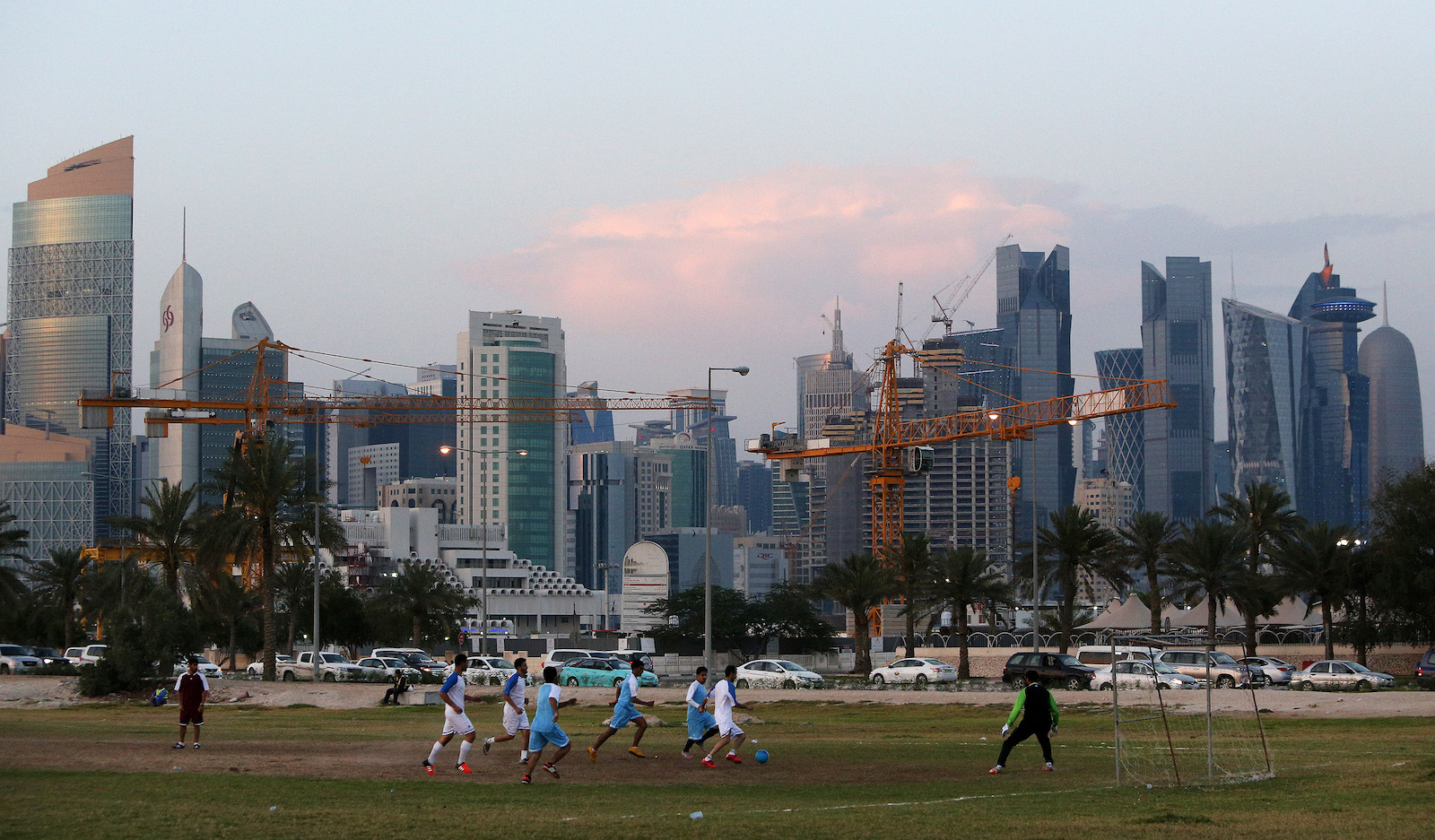 People playing soccer under a skyline punctuated by construction cranes